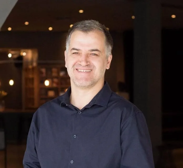 Smiling man in a dark shirt indoors.