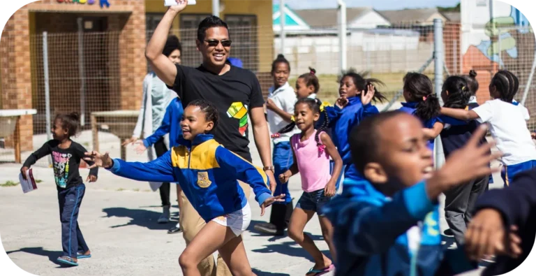 Children and adult playing outdoors, smiling and running.