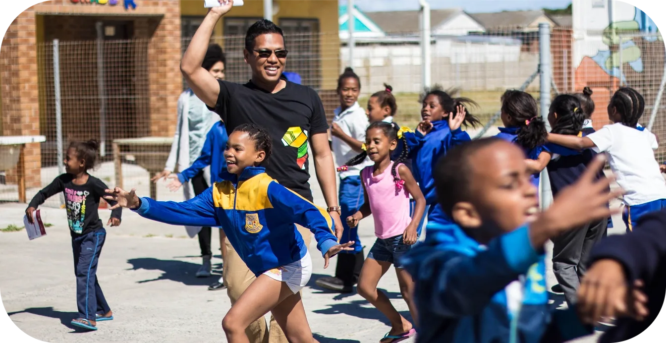 Children and adult playing outdoors, smiling and running.